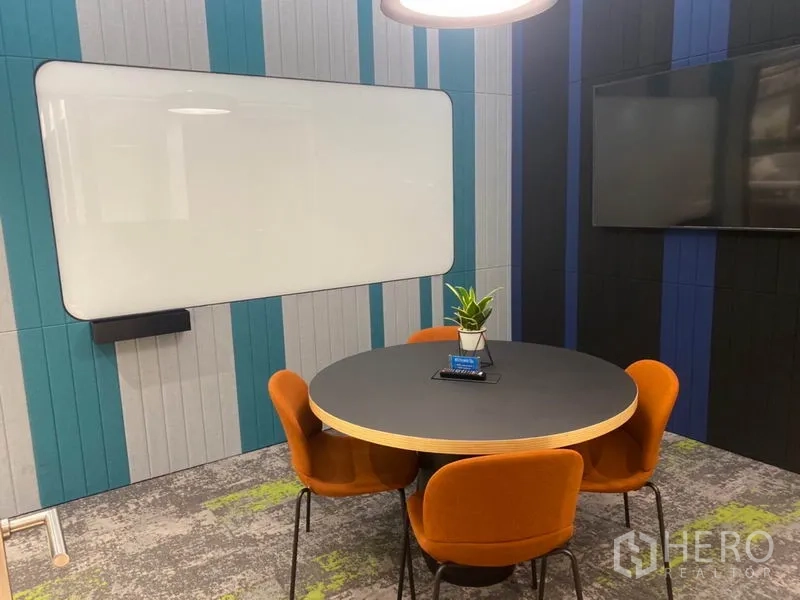 办公空间 出租在Pathum Wan, Bangkok - 小型洽谈室，圆桌、橙色椅子、白板与壁挂屏幕。