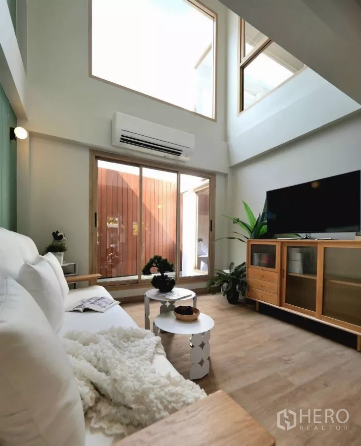 ทาวน์เฮาส์ ให้เช่าในWatthana, Bangkok - ห้องนั่งเล่นสว่างด้วยหน้าต่างสูงและประตูบานเลื่อน โซฟาสีขาวและตู้วางทีวีไม้