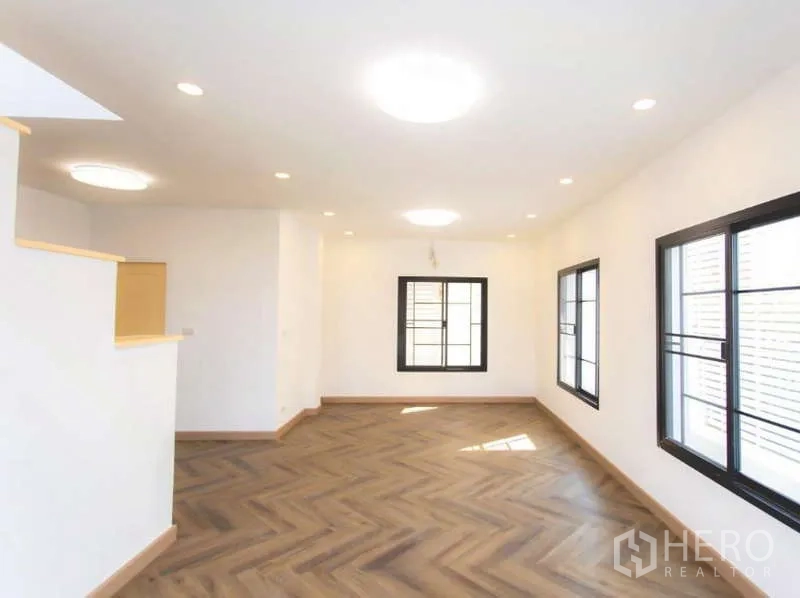 Detached House for sale in Wang Thonglang, Bangkok - Spacious upper-floor room with multiple black-framed windows and herringbone wood floors.