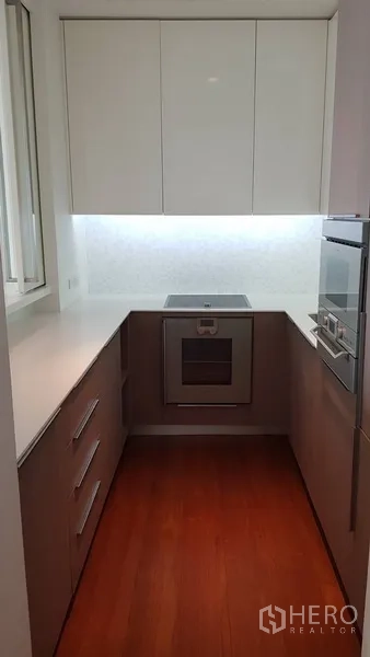 Condominium for rent in Pathum Wan, Bangkok - Compact U-shaped kitchen with cooktop, oven and ample storage.