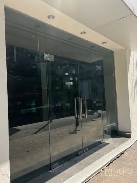 พื้นที่ขายปลีก ให้เช่าในKhlong Toei, Bangkok - หน้าร้านกระจกชั้นล่างพร้อมประตูกระจกคู่และไฟดาวน์ไลท์บริเวณทางเข้า.