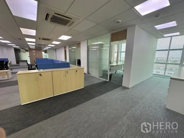 Office Space for rent - Bright office corridor showing cubicles, glass-partitioned rooms, storage cabinets and large windows.