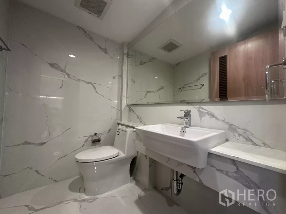 Townhouse for rent in Watthana, Bangkok - Bathroom with marble-effect tiles, wide mirror, vanity sink and toilet.