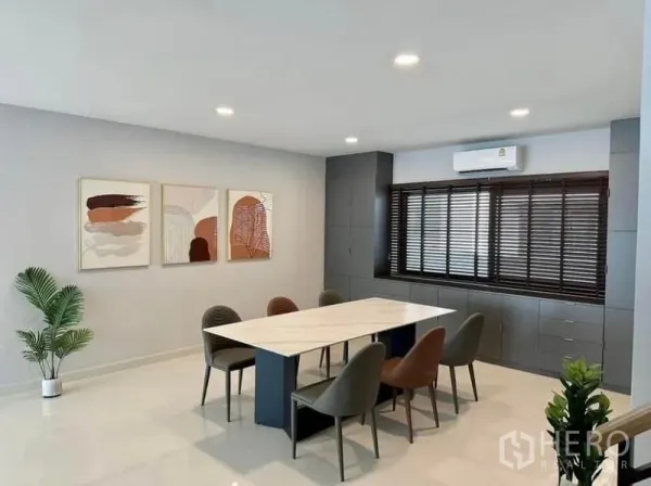 Detached House for rent in Bang Phli, Samut Prakan - Spacious dining area with long table, six chairs, wall art and built-in cabinetry beneath window blinds.