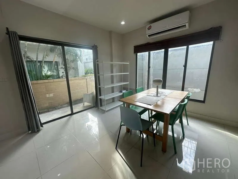 Detached House for rent or sale in Bang Kapi, Bangkok - Bright dining area with wooden table, multiple chairs, air conditioner and sliding doors to the garden.