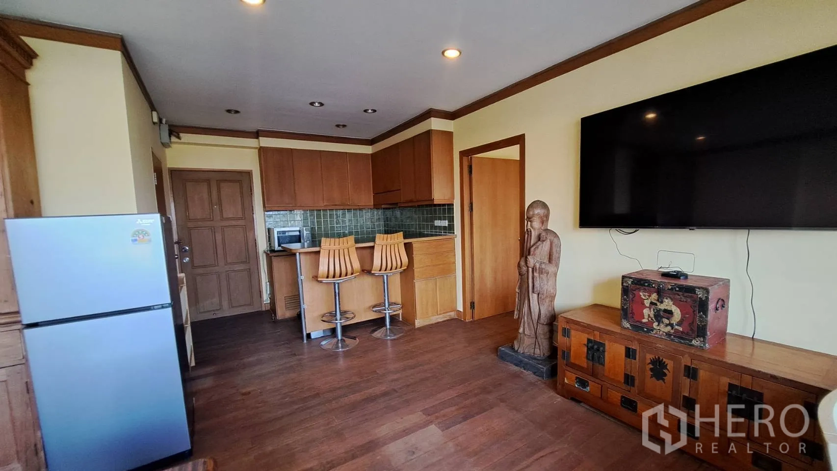 Condominium for rent in Khlong Toei, Bangkok - Open-plan living area with wall-mounted TV, refrigerator, and wooden console.