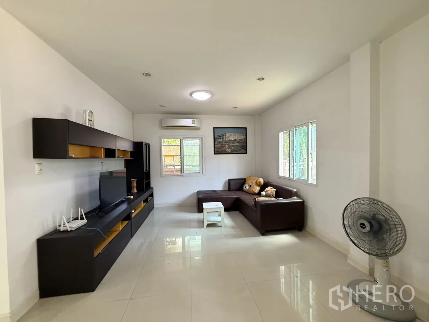 Detached House for rent in Lam Luk Ka, Pathum Thani - Living room with L-shaped sofa, wall-mounted cabinets, TV, and windows.