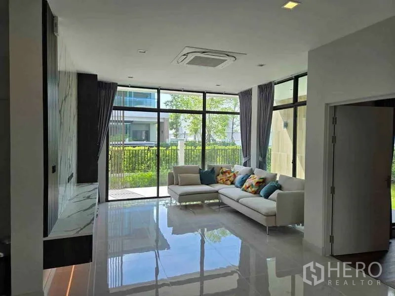 บ้าน ให้เช่าในBang Phli, Samut Prakan - ห้องนั่งเล่นกระจกเต็มบาน โซฟา L‑shape พื้นกระเบื้องเงา เชื่อมต่อสวน