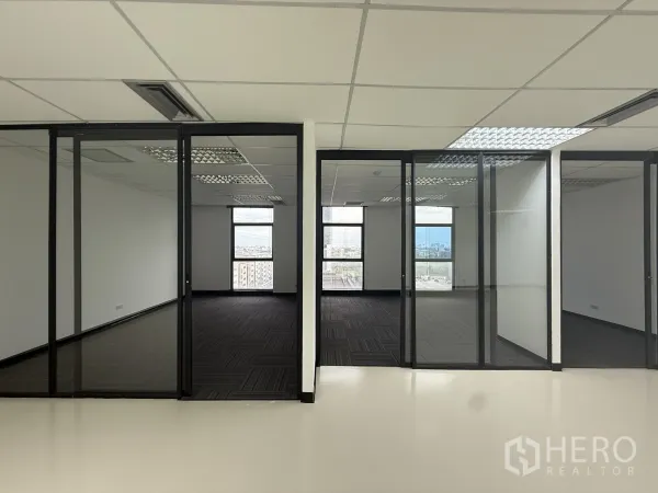 Office Space for rent - Row of glass-walled private offices with dark carpet tiles and large windows offering city views.