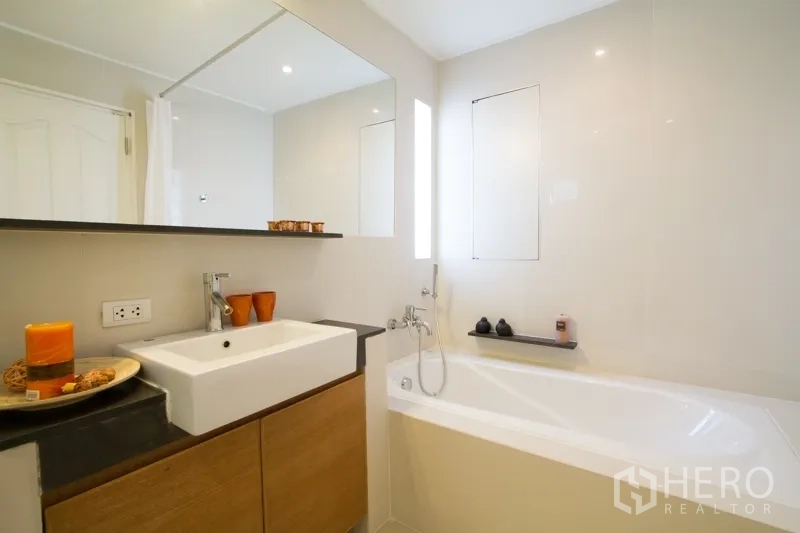 อพาร์ทเมนท์ ให้เช่าในWatthana, Bangkok - ห้องน้ำพร้อมอ่างอาบน้ำสีขาว กระจกบานใหญ่ และอ่างล้างหน้าทรงสี่เหลี่ยมบนตู้ไม้