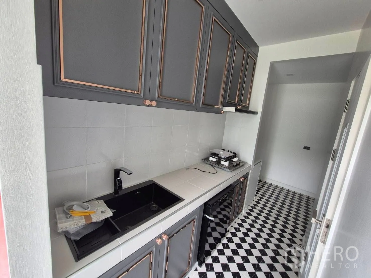 บ้าน ขายในBang Kruai, Nonthaburi - ครัวแบบแกลลี ตู้สีเทา อ่างล้างจานสีดำ เตาแก๊ส และพื้นกระเบื้องลายตาราง