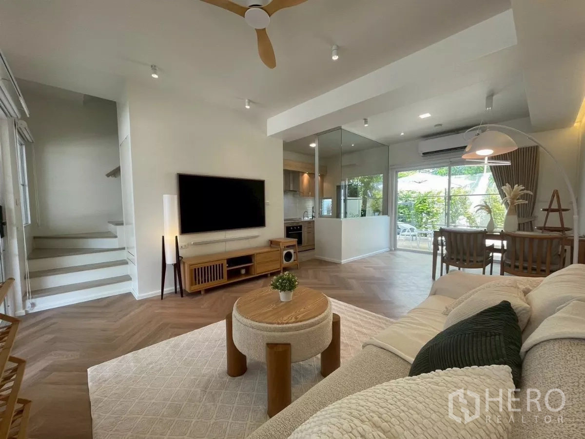 联排别墅 出租在Prawet, Bangkok - 明亮客厅，电视墙、用餐区、玻璃隔断厨房与花园景观。