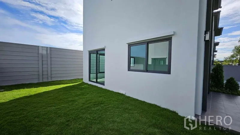 Detached House for sale in Samut Prakan - Private lawn wrapping the side of the house with sliding windows and high privacy wall.