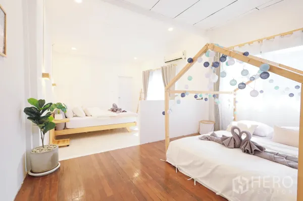 Townhouse for rent in Din Daeng, Bangkok - Spacious bedroom with wooden flooring, two beds and playful string lights by large windows.