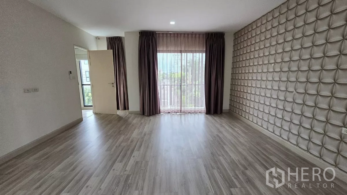 Townhouse for rent or sale in Saphan Sung, Bangkok - Spacious master bedroom with 3D feature wall and sheer curtains to a balcony.