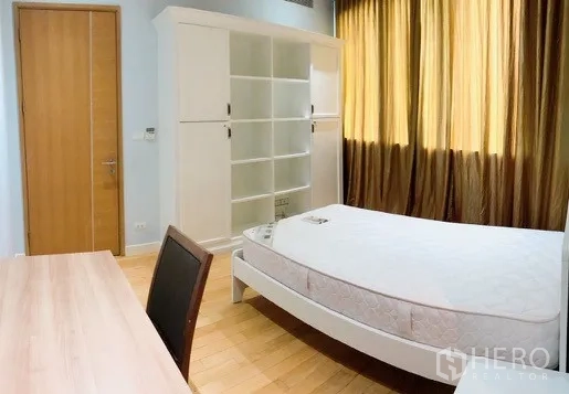 Condominium for rent or sale in Khlong Toei, Bangkok - Second bedroom featuring a work desk, white shelving unit and full-length curtains.