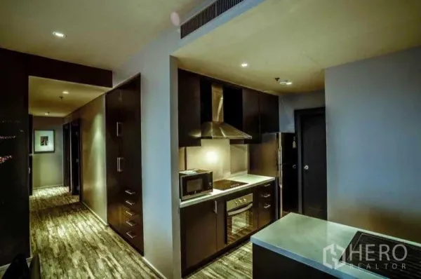 คอนโด ให้เช่าหรือขายในKhlong Toei, Bangkok - ครัวแบบแกลลีย์สมัยใหม่พร้อมเตาอบ เตาไฟฟ้า เครื่องดูดควัน และตู้บิ้วท์อินโทนเข้มตามแนวทางเดิน