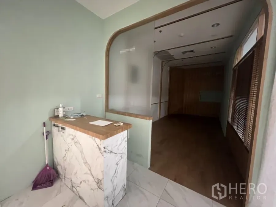 พื้นที่ขายปลีก ให้เช่าในWatthana, Bangkok - มุมต้อนรับพร้อมเคาน์เตอร์ลายหินอ่อน ผนังสีเขียวมิ้นต์ กระจกฝ้า และพื้นที่ขายพื้นไม้ถัดเข้าไป.