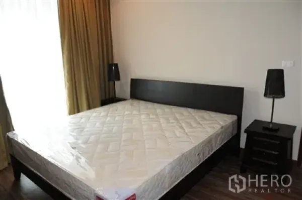 公寓 出租在Khlong Toei, Bangkok - 卧室配大床、床头柜与台灯，临近窗帘大窗。