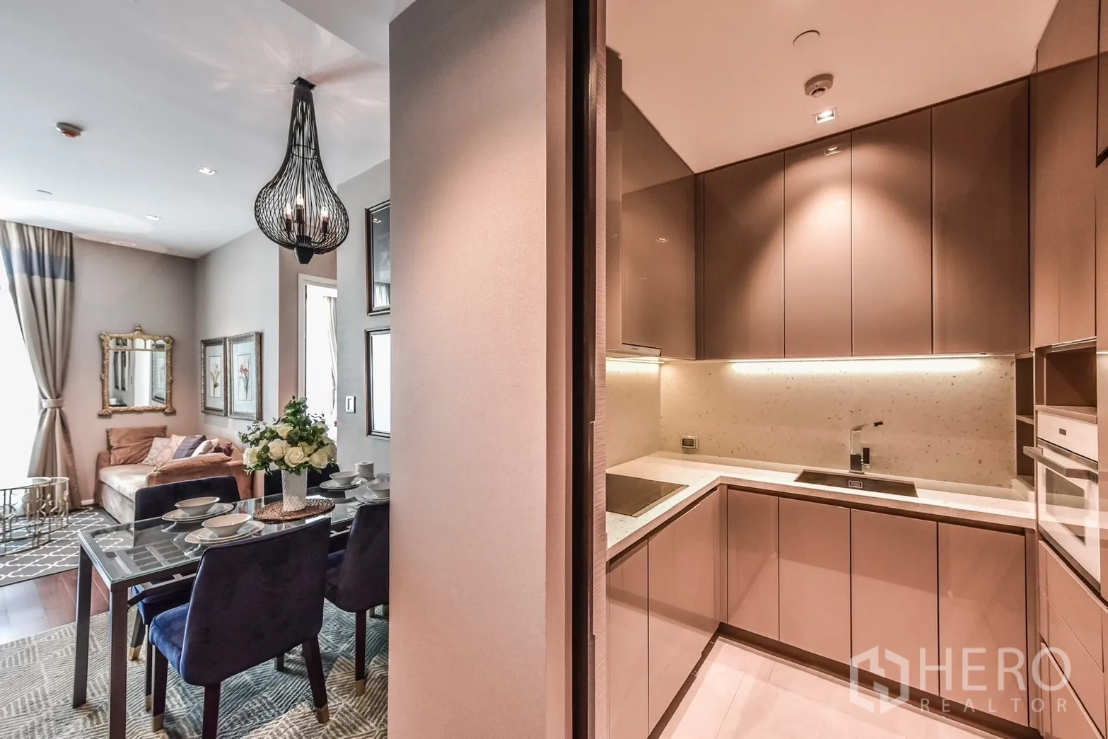 Condominium for rent or sale in Watthana, Bangkok - Modern U-shaped kitchen with glossy cabinetry, built-in hob and under-cabinet lighting next to the dining area.