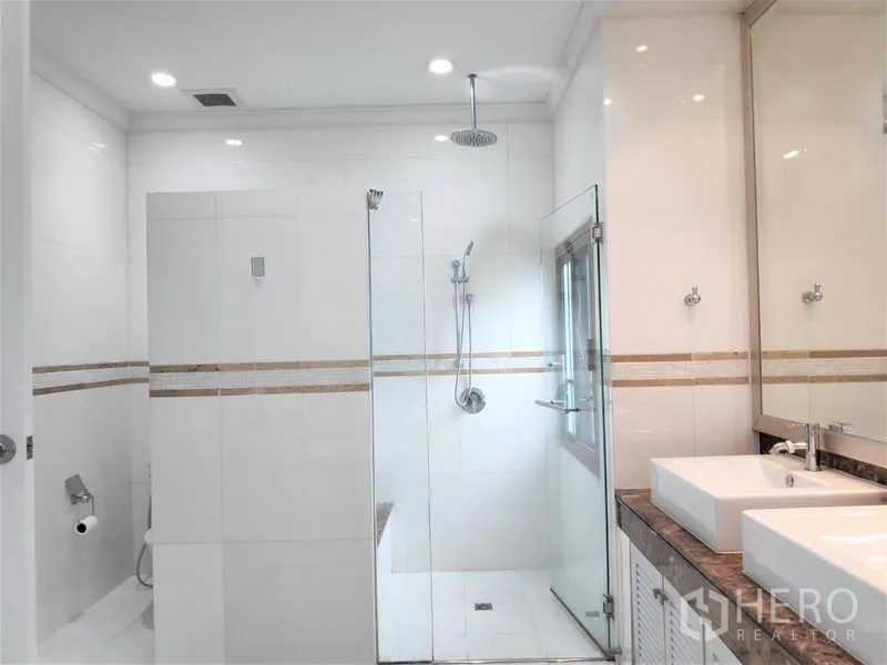 独立式住宅 出租在Watthana, Bangkok - 明亮浴室，玻璃淋浴间配顶喷花洒，双台盆与现代洁具。