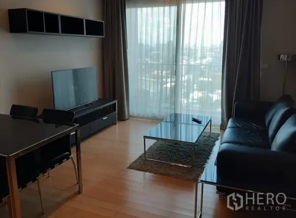 คอนโด ให้เช่าในKhlong Toei, Bangkok - ห้องนั่งเล่นโปร่ง แสงธรรมชาติ โซฟาหนัง โต๊ะกลางกระจก ชั้นวางทีวี และหน้าต่างสูงวิวเมือง