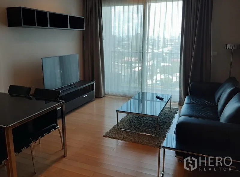 คอนโด ให้เช่าในKhlong Toei, Bangkok - ห้องนั่งเล่นโปร่ง แสงธรรมชาติ โซฟาหนัง โต๊ะกลางกระจก ชั้นวางทีวี และหน้าต่างสูงวิวเมือง