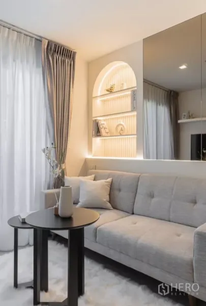 Condominium for rent in Chatuchak, Bangkok - Close‑up of the living corner with soft rug, nesting tables and illuminated arch shelving.