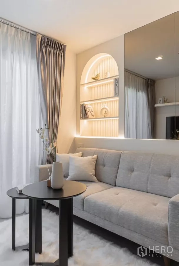 Condominium for rent in Chatuchak, Bangkok - Close‑up of the living corner with soft rug, nesting tables and illuminated arch shelving.