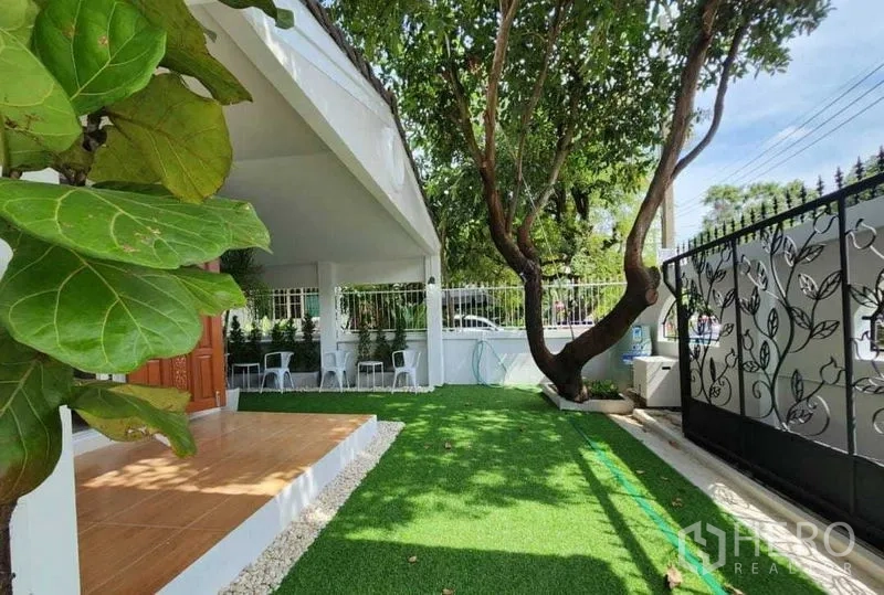 บ้าน ให้เช่าในLam Luk Ka, Pathum Thani - สวนหน้าบ้านมีต้นไม้ใหญ่ หญ้าเทียม และประตูเหล็กดัด