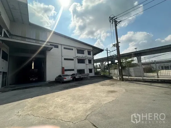 Warehouse for rent in Suan Luang, Bangkok - Warehouse exterior with wide driveway, parking area and nearby elevated rail in Suan Luang, Bangkok.