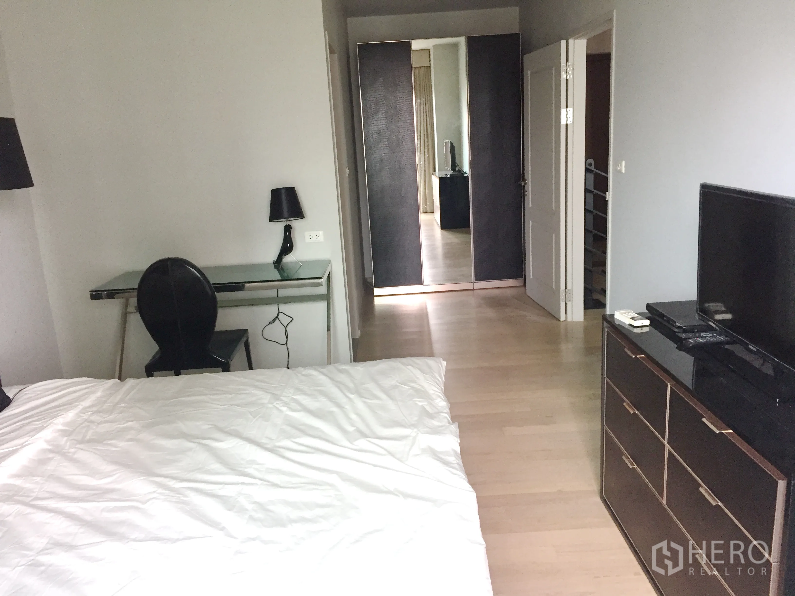 คอนโด ให้เช่าในBangkok - มุมมองห้องนอนพร้อมตู้เสื้อผ้าบานกระจก โต๊ะทำงาน ชั้นวางทีวี และพื้นไม้โทนอ่อน