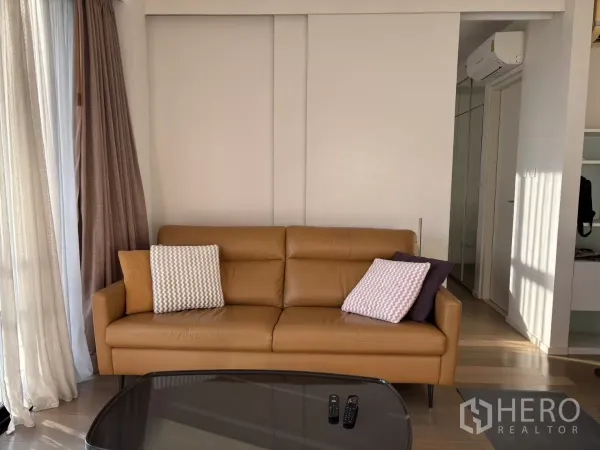 Condominium for sale in Watthana, Bangkok - Cozy tan leather sofa in the living area with sliding panels and hallway to bedroom.