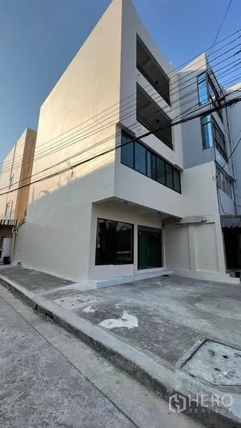 Shophouse for rent in Bang Kapi, Bangkok - Corner shophouse exterior with large glass windows and a small parking forecourt.