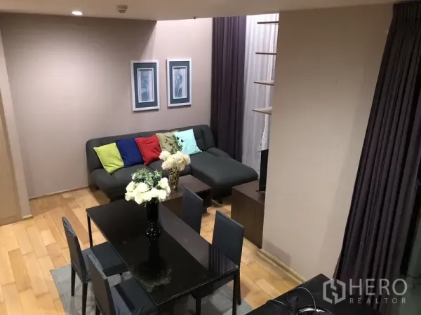 คอนโด ให้เช่าหรือขายในKhlong San, Bangkok - มุมมองจากชั้นลอยเห็นห้องนั่งเล่นและรับประทานอาหาร พร้อมหมอนสีสันและผ้าม่านสูง