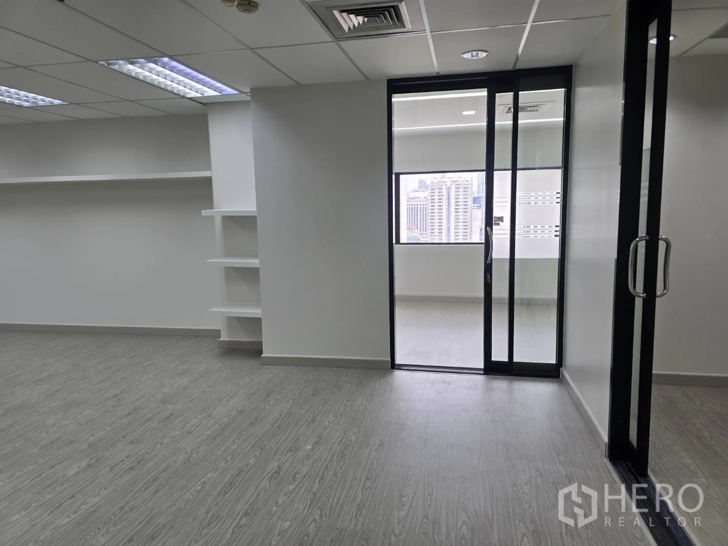 Office Space for rent in Khlong Toei, Bangkok - Workspace leading to a glass-partitioned room with wall-mounted shelves.