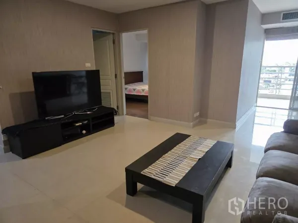 คอนโด ให้เช่าในKhlong Toei, Bangkok - ห้องนั่งเล่นกว้างพร้อมชั้นวางทีวี โต๊ะกลาง และทางเข้าห้องนอนกับระเบียง