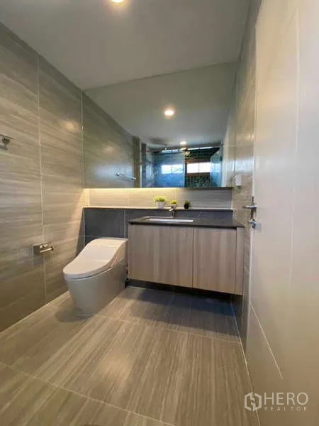 Detached House for rent in Bang Kapi, Bangkok - Second bathroom with long wall mirror, vanity and gray floor tiles.