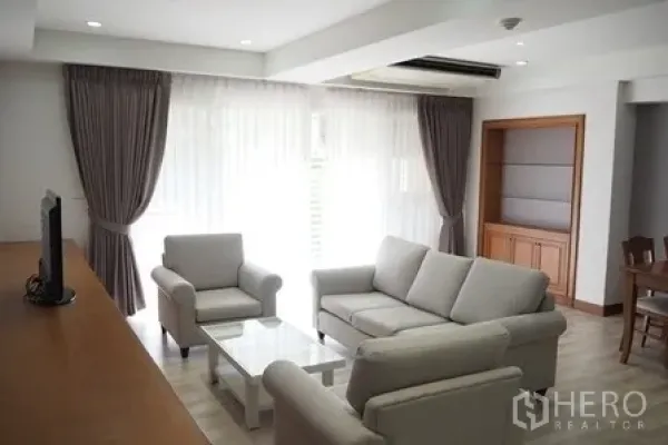 Condominium for rent in Pathum Wan, Bangkok - Living area with large windows, sheer curtains and a grey sofa set.