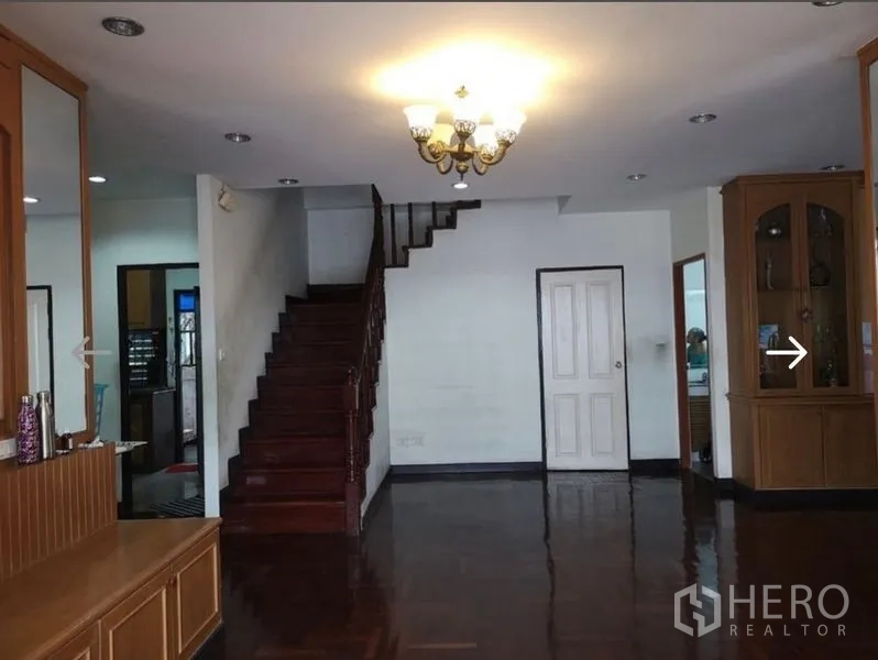 Detached House for sale in Khlong San, Bangkok - Living room with polished wooden floors and a staircase leading upstairs.
