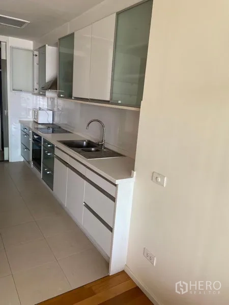 公寓 出租在Khlong Toei, Bangkok - 走廊式厨房，白色橱柜、水槽、灶台与烤箱。