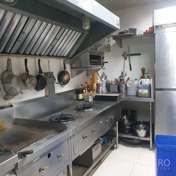 零售空间 出租在Khlong Toei, Bangkok - 商业厨房，带排烟罩、炉灶、煎台及悬挂锅具，白色瓷砖墙面。