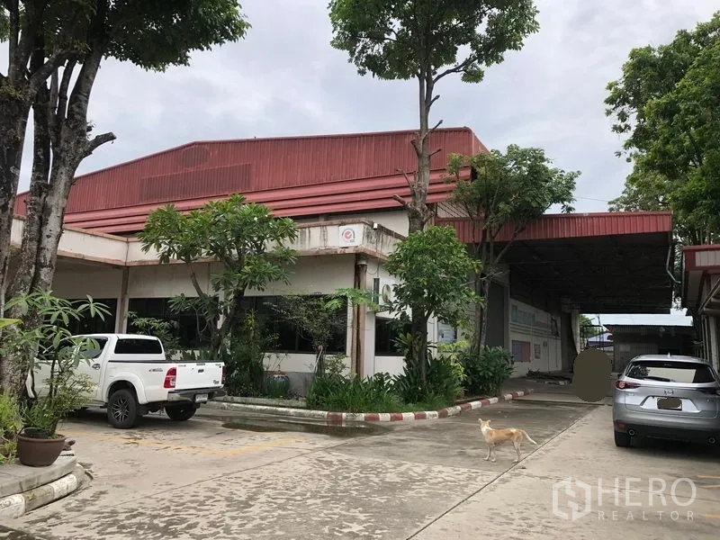 工厂 出售在Lam Luk Ka, Pathum Thani - 工厂外观，红色屋顶，宽阔车道与停车区，绿化环绕