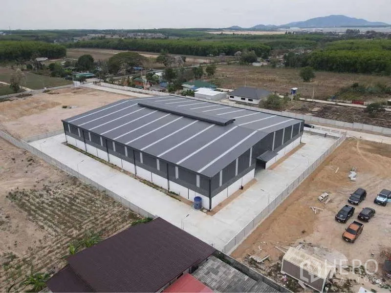 คลังสินค้า ให้เช่าหรือขายในNikhom Phatthana, Rayong - ภาพมุมสูงด้านหลัง แสดงตัวอาคารโกดัง ทางวิ่งคอนกรีต และพื้นที่สีเขียวโดยรอบในระยอง