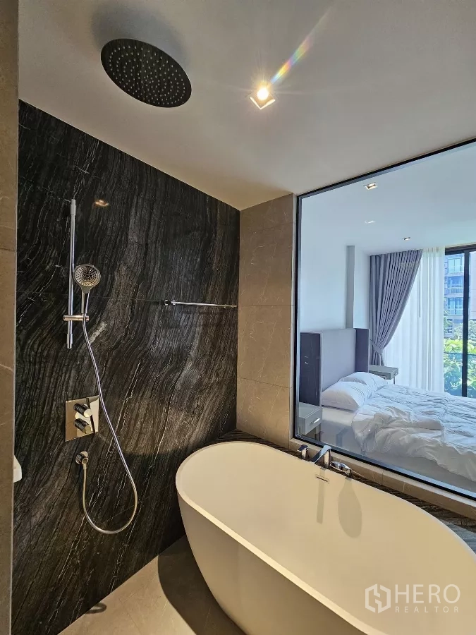 公寓 出租在Watthana, Bangkok - 雨淋花洒与独立浴缸，深色石材强调墙。