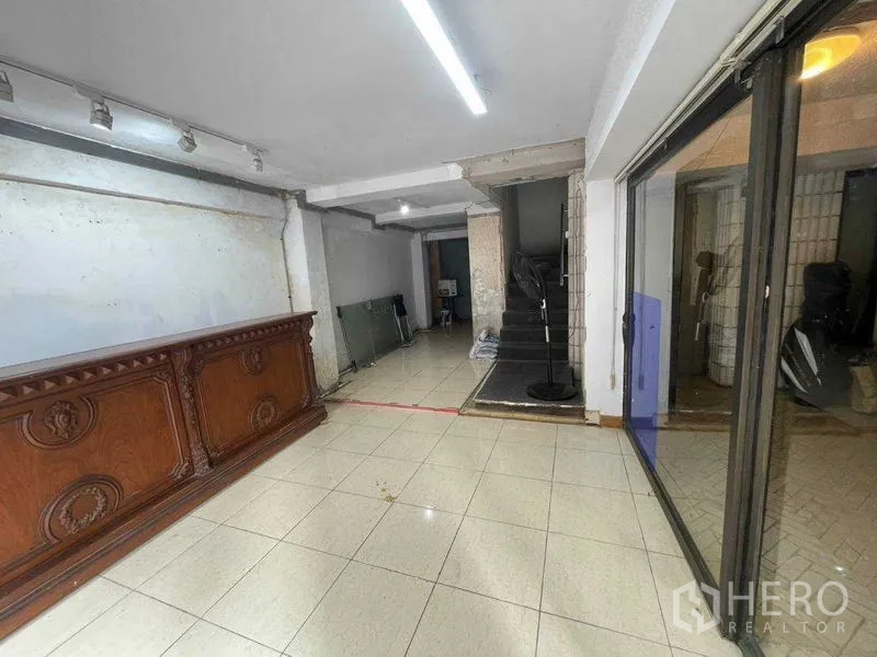 店屋 出租在Bang Rak, Bangkok - 铺面内部铺砖地面，木质前台、轨道灯与室内楼梯。