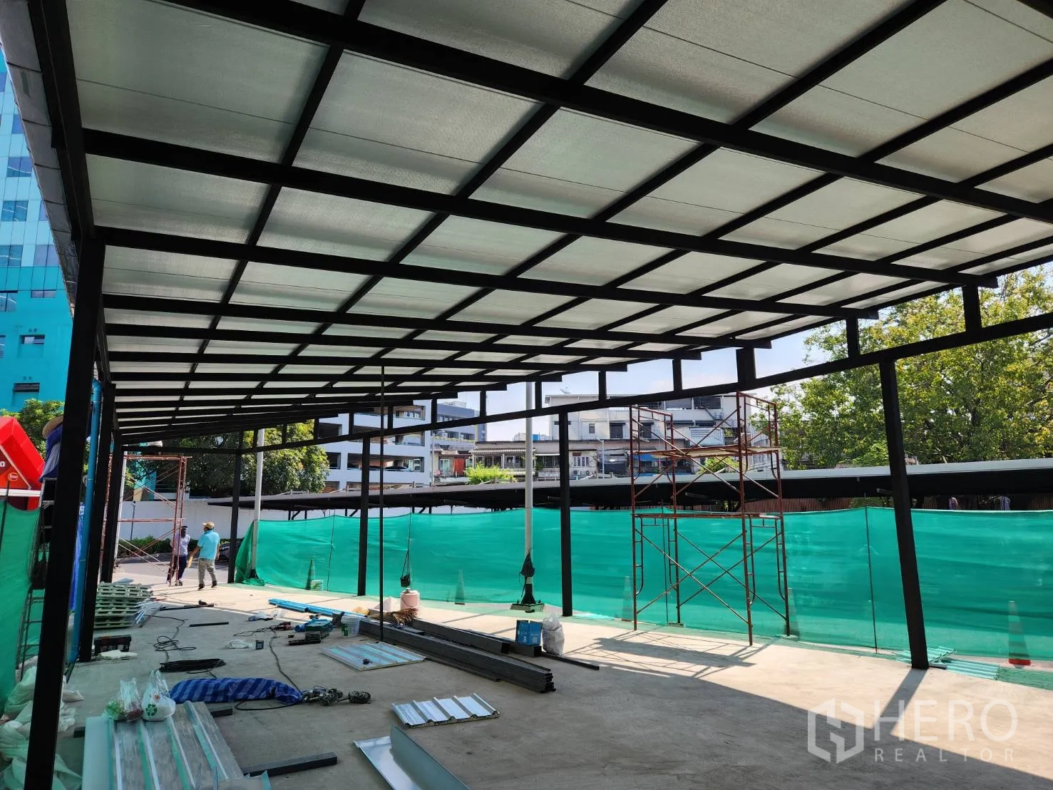 零售空间 出租在Khlong Toei, Bangkok - 棚架内部视角，宽阔开放式地面与钢格栅屋顶，采光充足，外围设绿色遮挡。