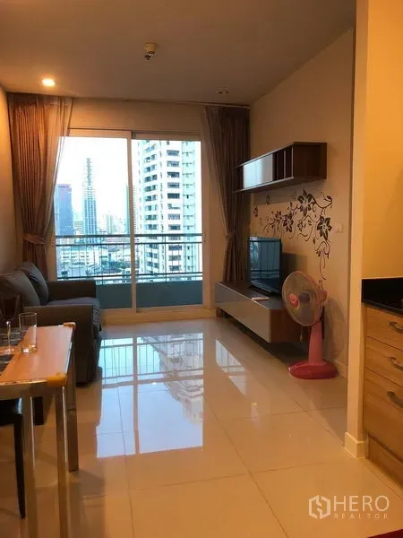 Condominium for sale in Ratchathewi, Bangkok - Bright living area with sliding doors to a balcony, city skyline view, wall shelves and a TV unit.