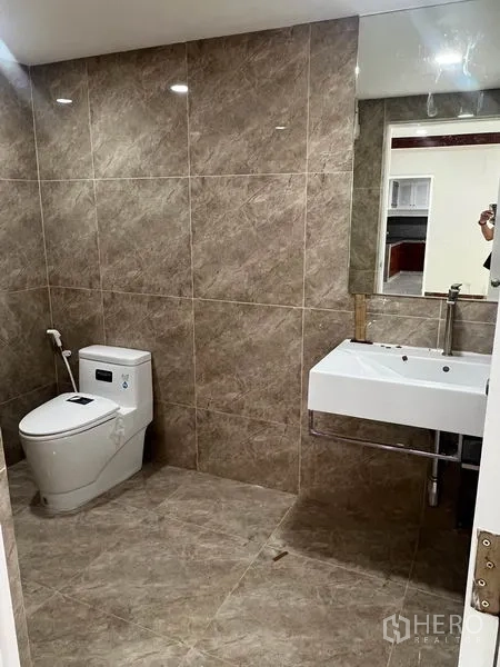 Townhouse for rent in Watthana, Bangkok - Bathroom with brown wall tiles, wall-mounted sink, and modern toilet.