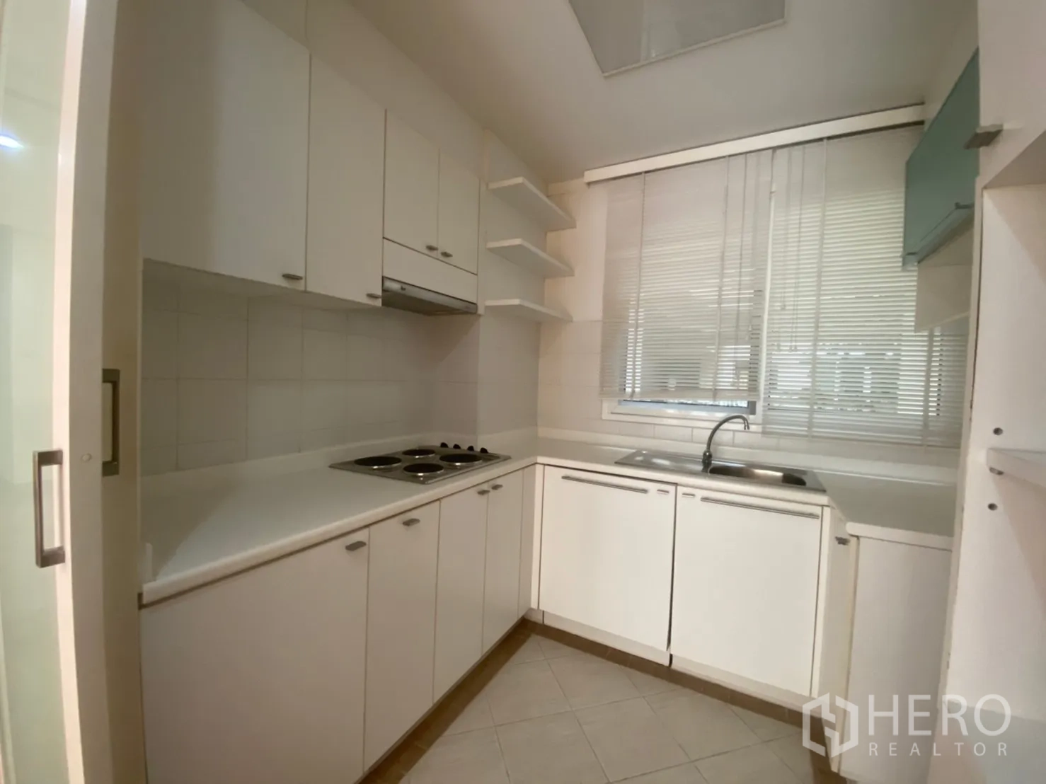 Condominium for rent or sale in Sathon, Bangkok - Compact U-shaped kitchen with white cabinetry, cooktop and window sink.
